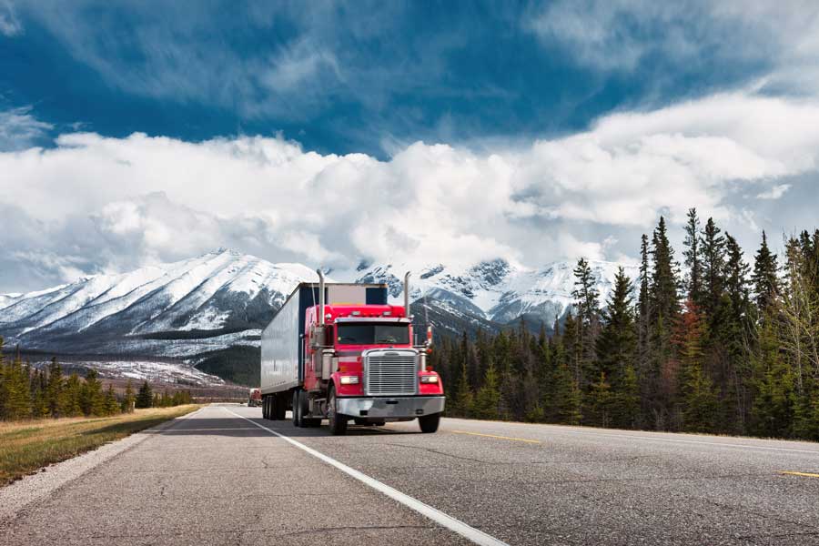 A red semi truck trailer drives his route in Canada.